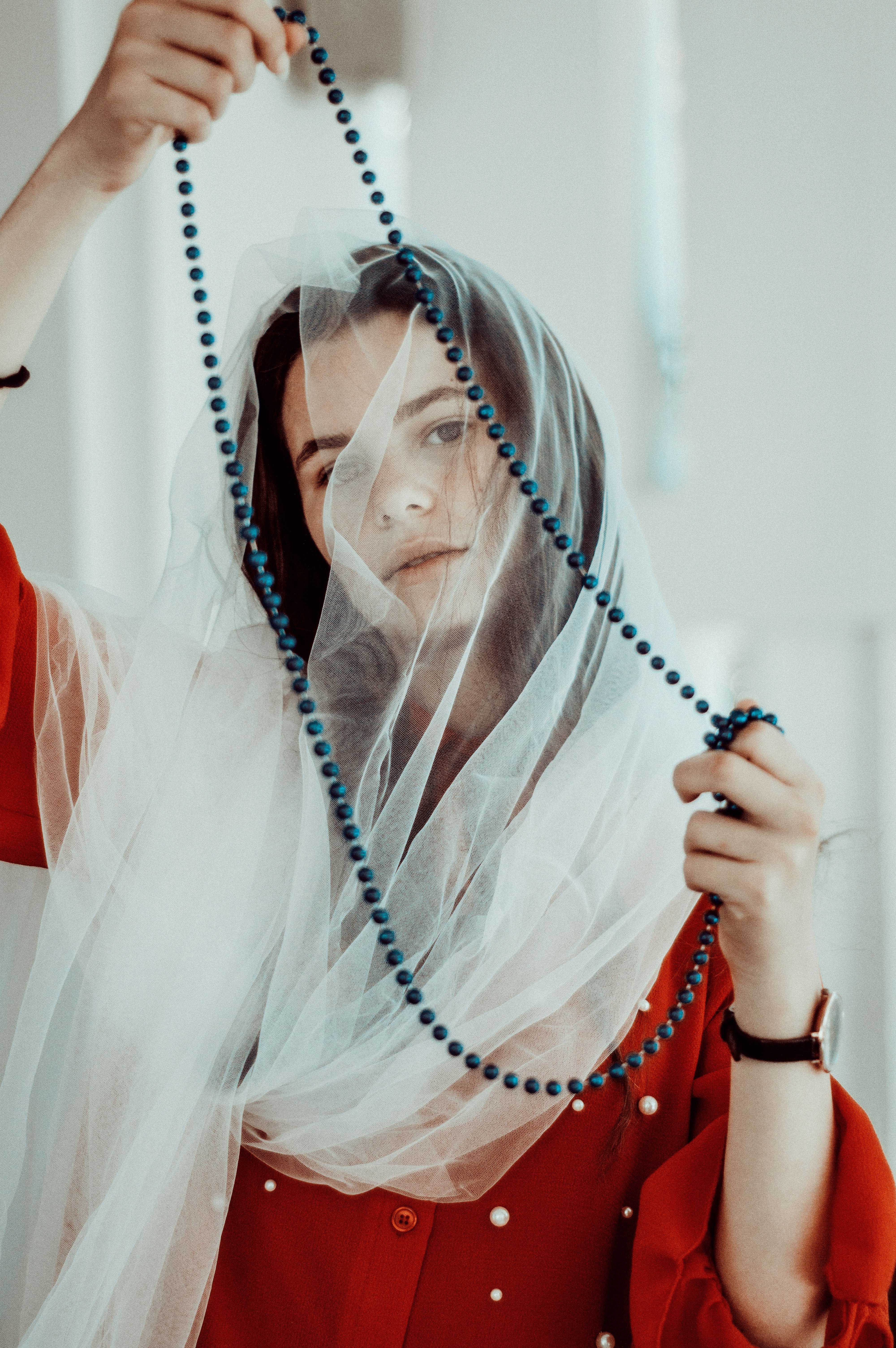 woman wearing white headdress and red dress holding black beaded necklace